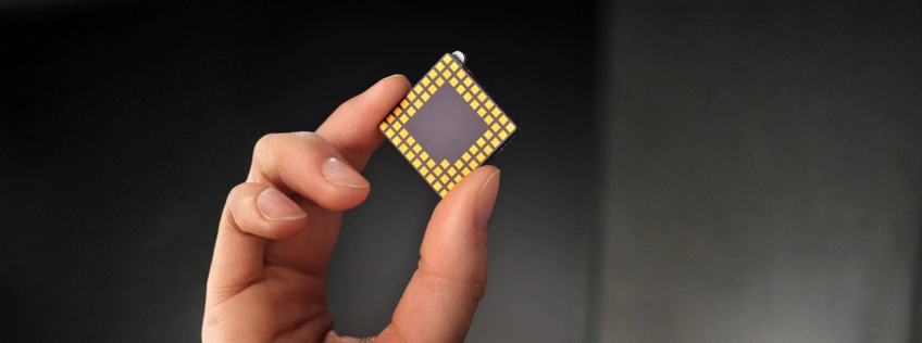 Dłoń trzymająca procesor komputerowy (CPU) z widocznymi złotymi pinami – zbliżenie na układ scalony na tle rozmytego tła.