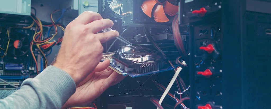 Montaż podzespołów komputerowych – ręce instalujące kartę graficzną lub pamięć RAM wewnątrz otwartej obudowy PC, widoczne okablowanie i wentylatory.